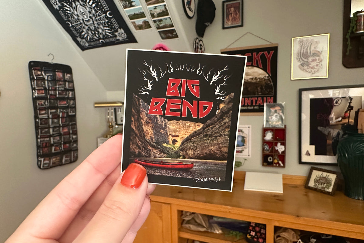 Person holding a 'Big Bend' sticker in front of a wall with framed pictures.