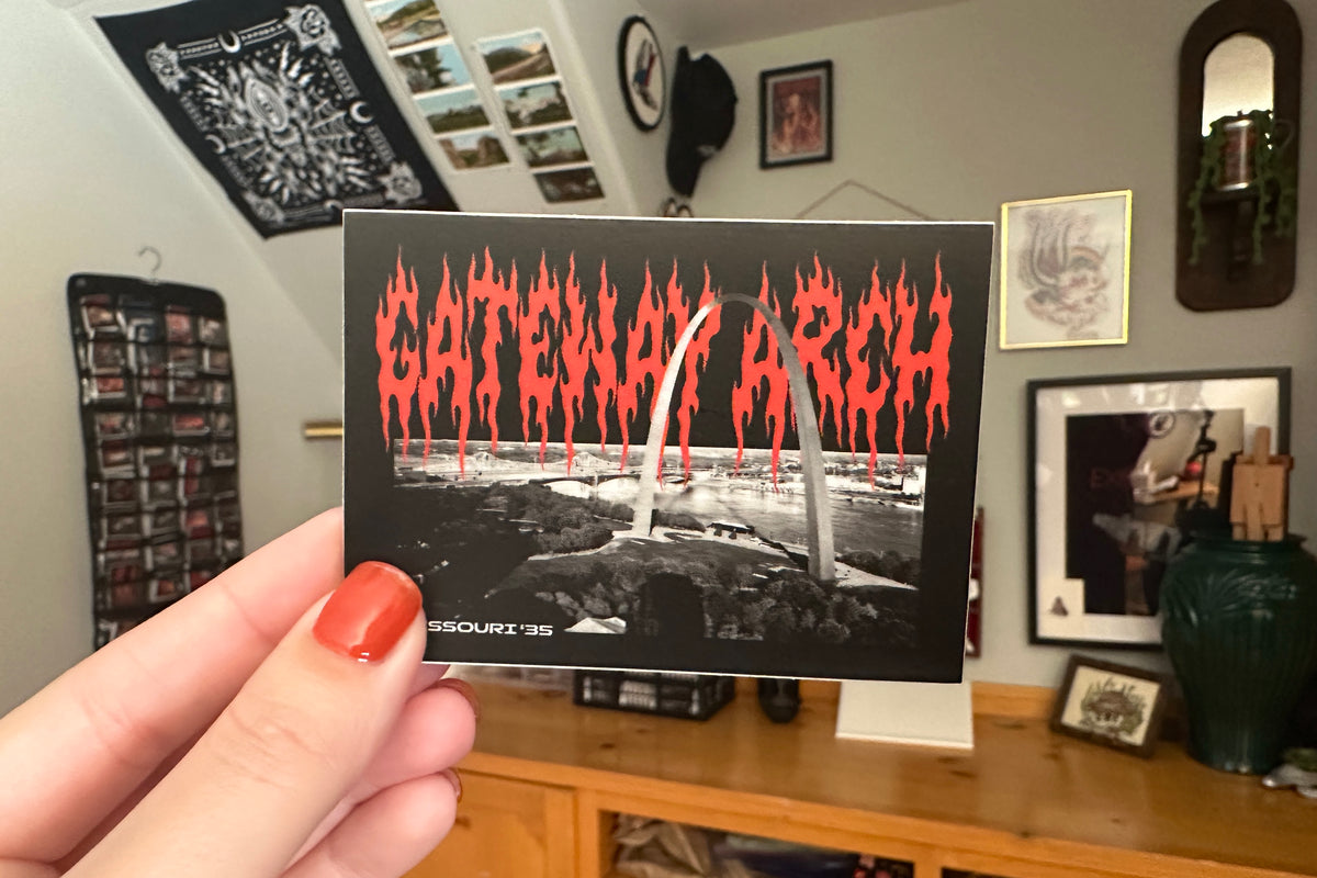 Person holding a 'Gateway Arch' sticker in a room with decor.
