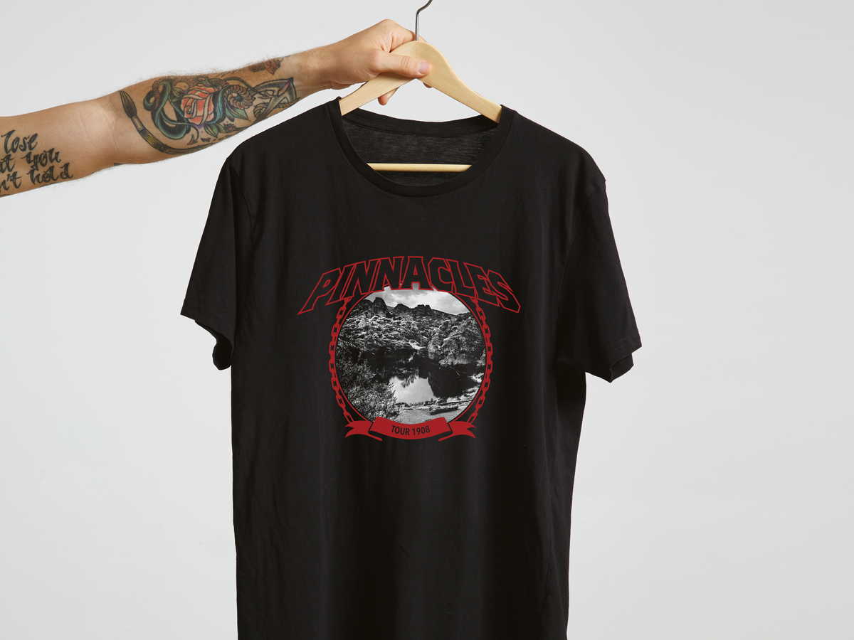 A black t-shirt with a red and white 'Pinnacles' design, on a hanger in front of a white background