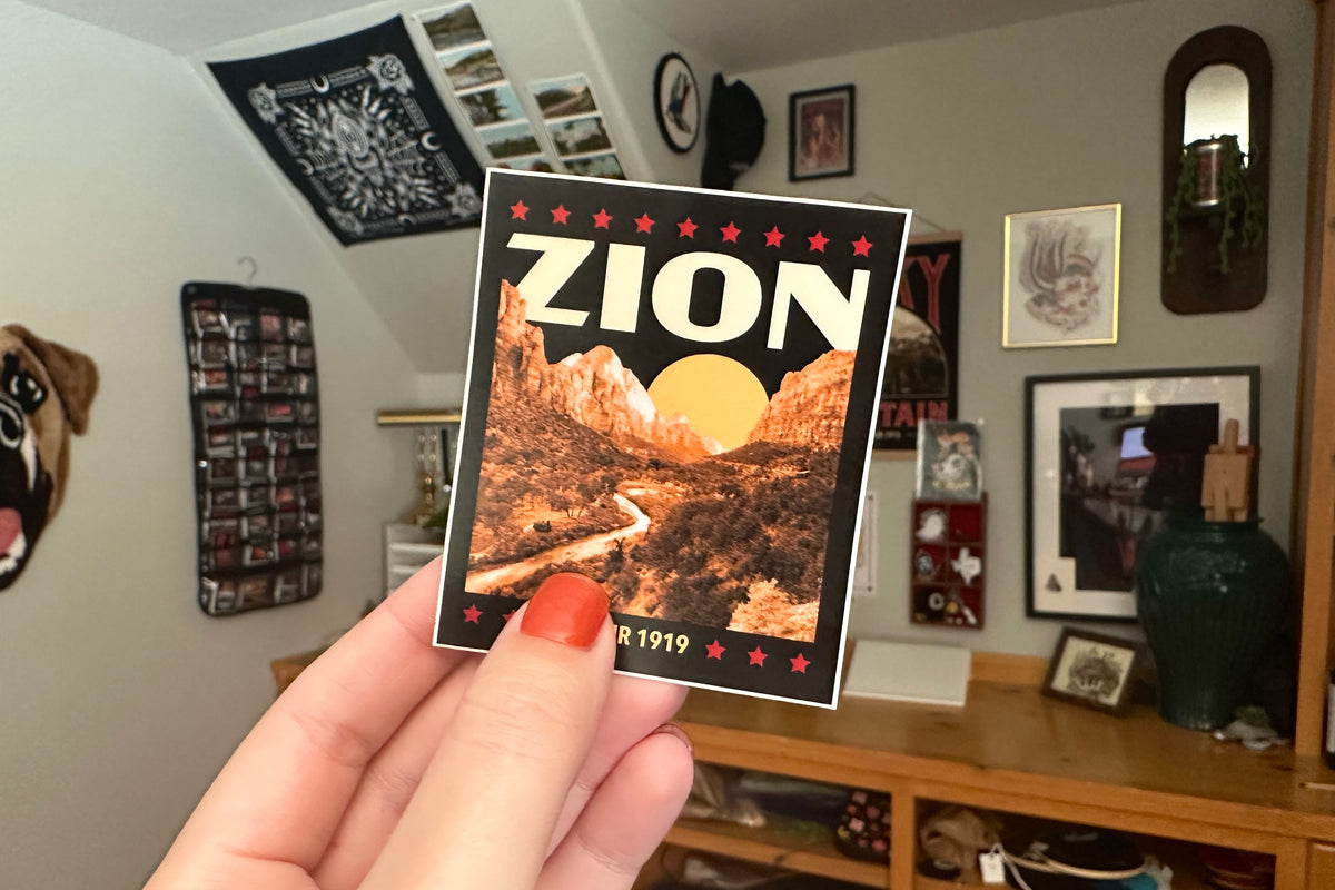 Hand holding a 'Zion' sticker in a room with various decorations.