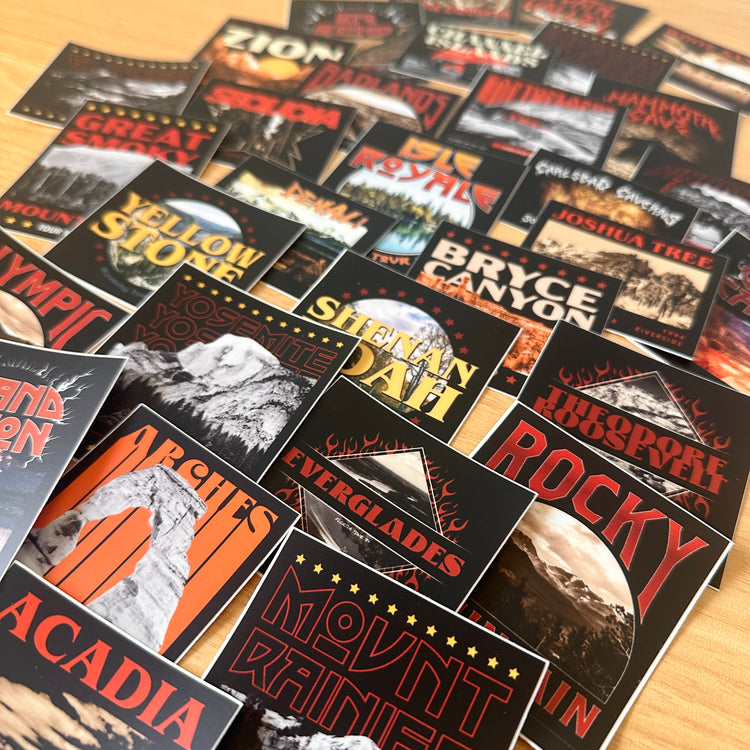 A pile of stickers showing imagery of various national parks. Shop our National Park Stickers—ideal gifts for national park lovers! Featuring unique, band merch-inspired designs that celebrate your favorite parks.