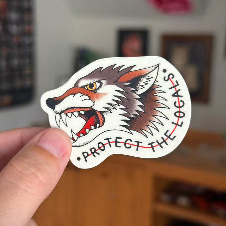 An American Traditional Tattoo Sticker depicting a grey wolf and the words 'Protect The Locals'. Perfect gifts for national park lovers who appreciate art and adventure!