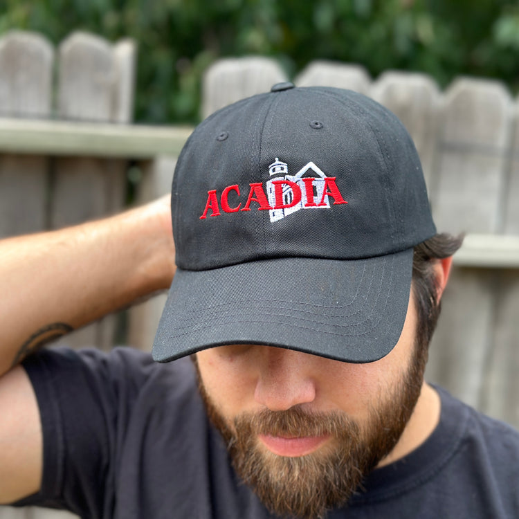 A man wearing a black hat with a lighthouse and the word 'Acadia' embroidered on it. Explore our National Park Hats, the perfect national parks apparel! Edgy, nature-themed designs inspired by band merch make great gifts from our national park gift store.