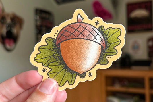 Sticker of an acorn held by a hand with a blurred indoor background