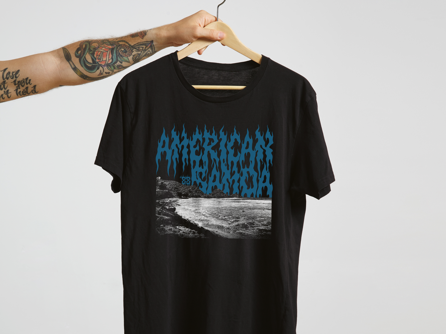 Black t-shirt with blue 'American Samoa' graphic design on a hanger against a white background