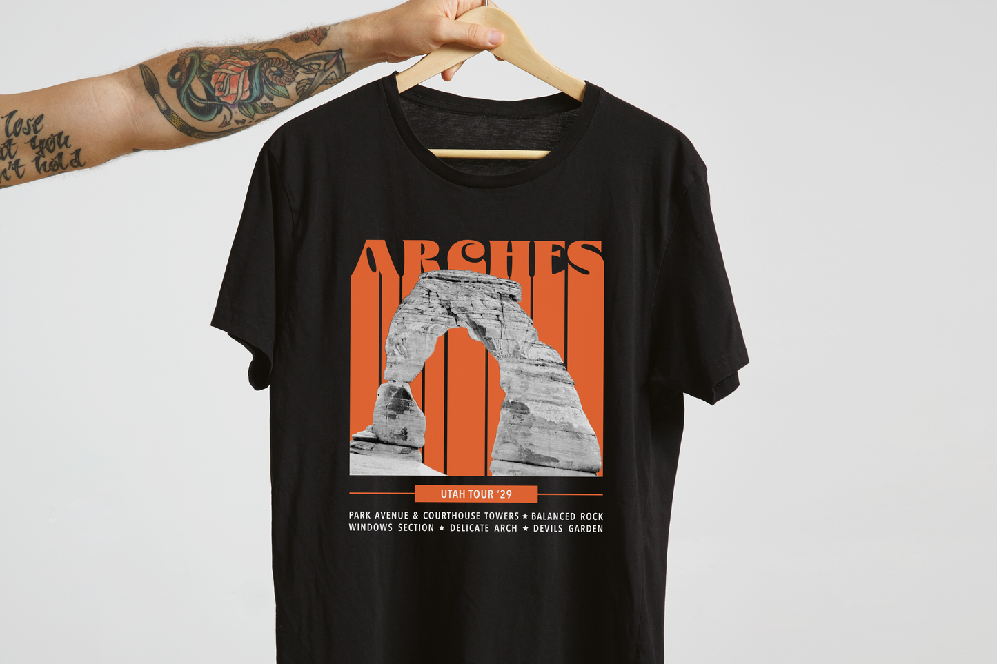 Black t-shirt with orange 'Arches' graphic design on a hanger against a white background