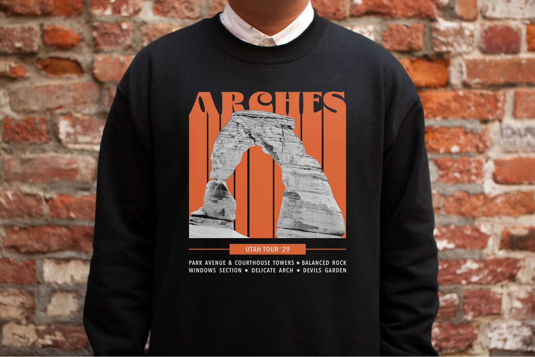 Person wearing a black sweatshirt with 'Arches' graphic against a brick wall.