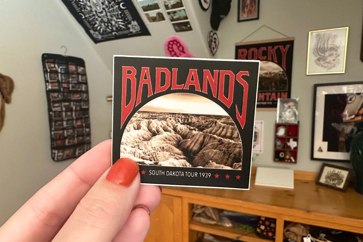 Hand holding a 'Badlands' sticker in a room.