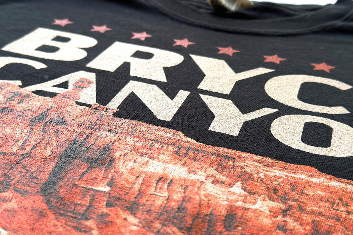 Black t-shirt with 'BRYCCE CANYON' printed on it, featuring an orange and white graphic design.