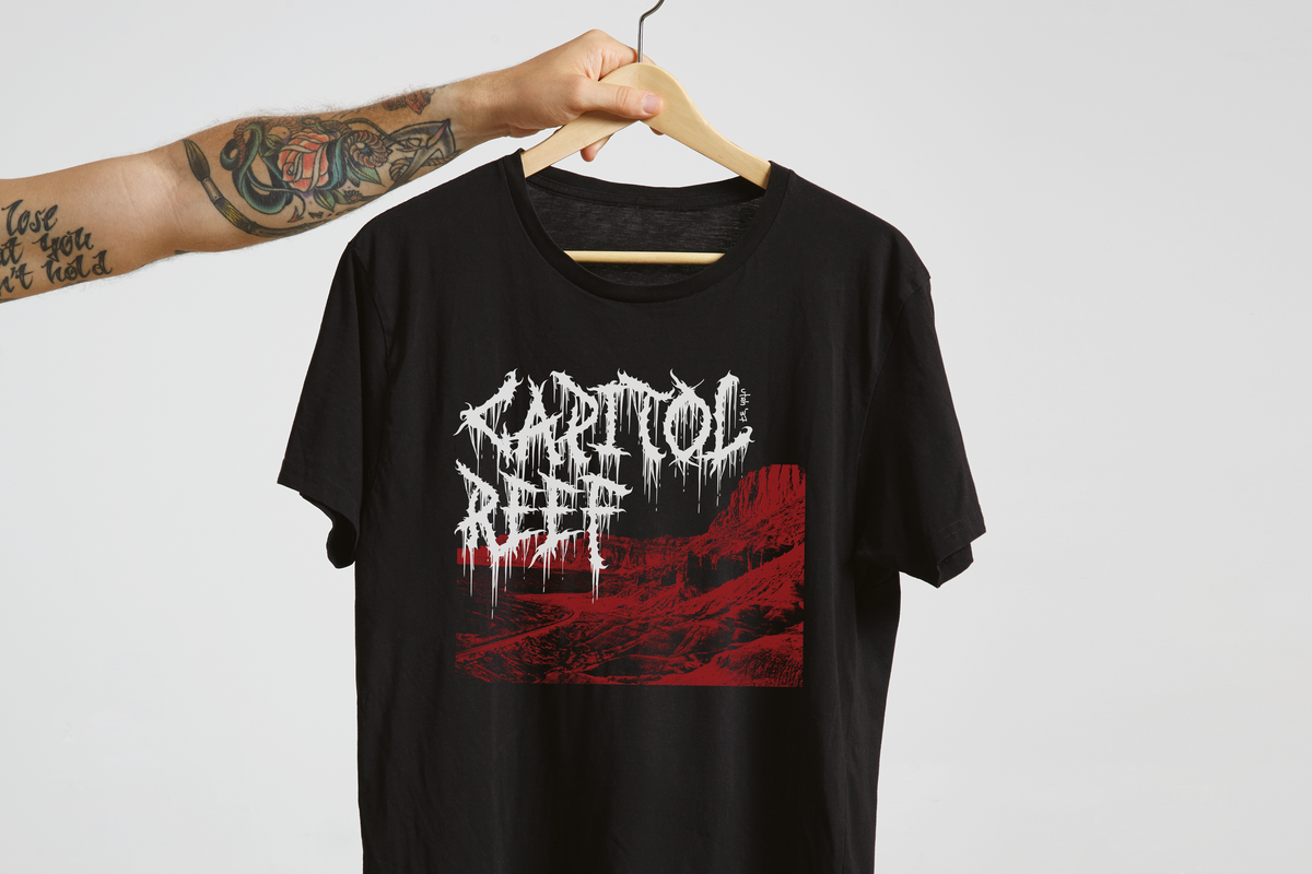 Black t-shirt with white and red 'Capitol Reef' graphic design on a hanger against a light gray background