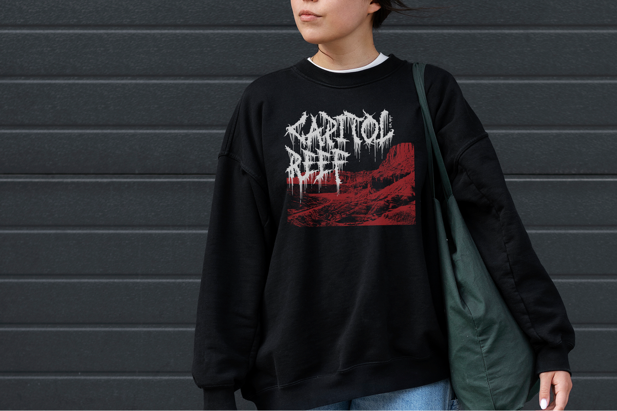 Person wearing a black sweatshirt with 'Capitol Reef' design against a gray wall.