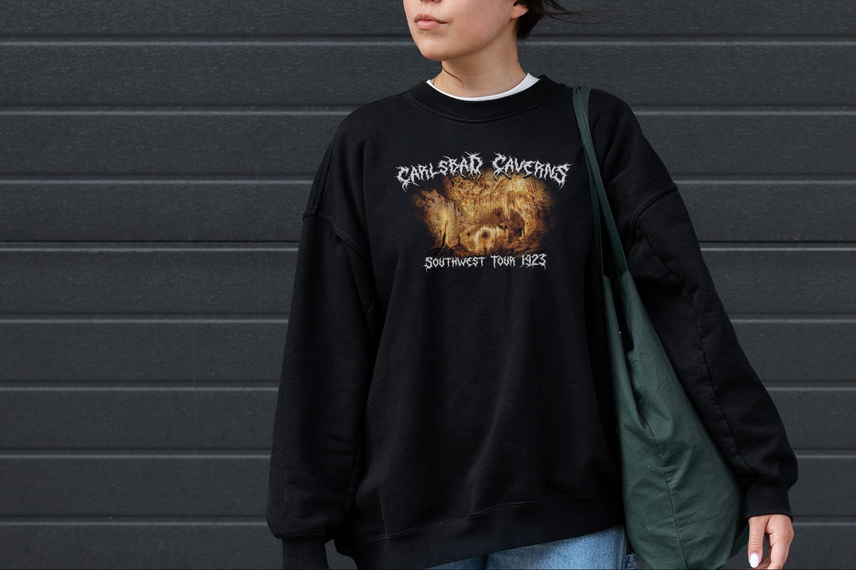 Person wearing a black sweatshirt with a 'Carlsbad Caverns' graphic design in front of a gray wall