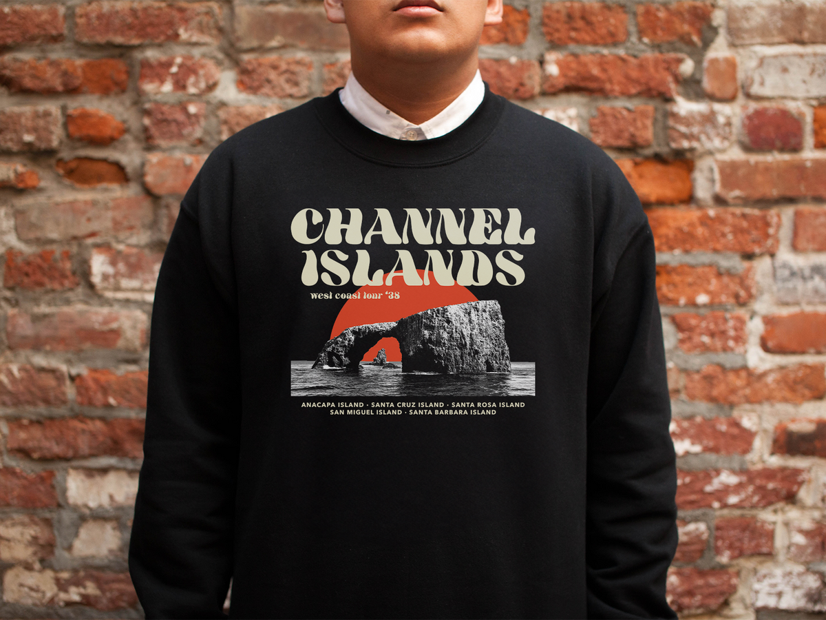 A person wearing a black sweatshirt with a 'Channel Islands' design, in front of a brick wall
