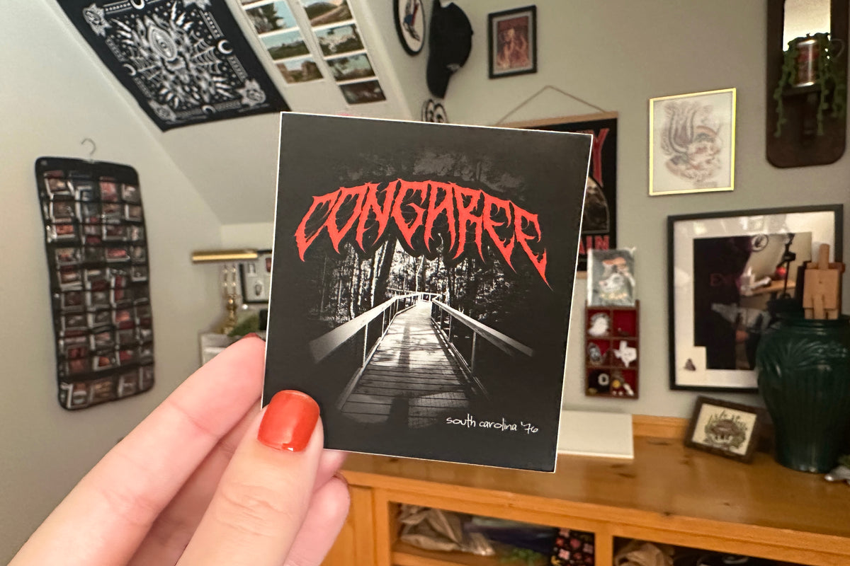 Person holding a 'Congaree' sticker in a room with framed pictures on the wall.