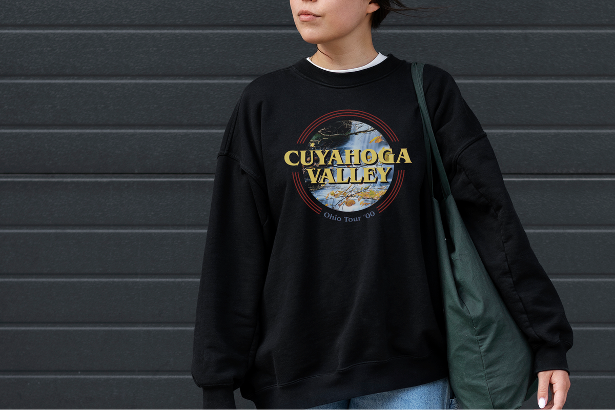 Person wearing a black sweatshirt with 'Cuyahoga Valley' print against a gray wall.