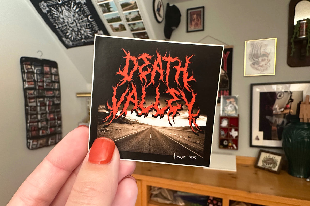 Hand holding a 'Death Valley' sticker in a room with decor.