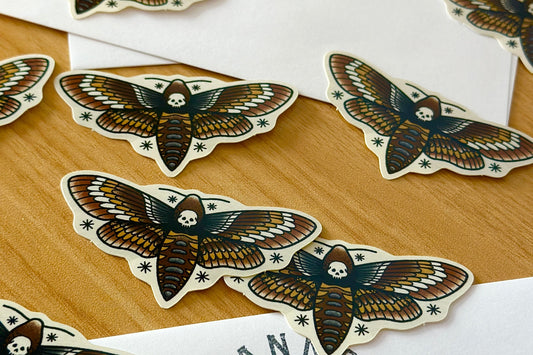Moth-shaped stickers with skull designs on a wooden surface
