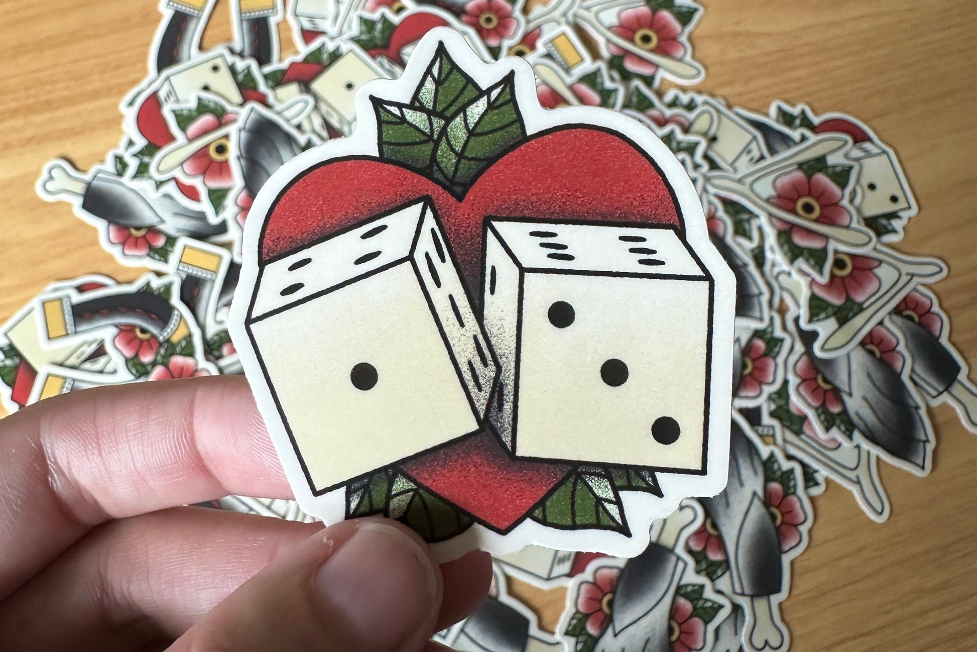 Sticker of two dice on a heart with additional stickers in the background on a wooden surface