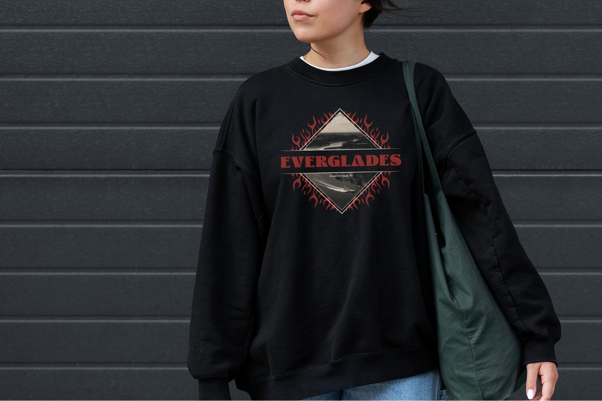 Person wearing a black sweatshirt with 'Everglades' design against a gray wall