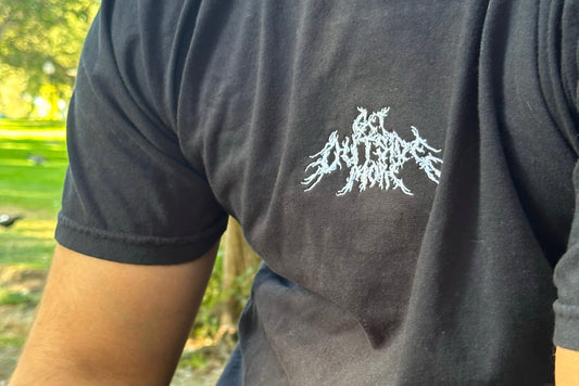 A person wearing a black t-shirt with a white design on a blurred outdoor background