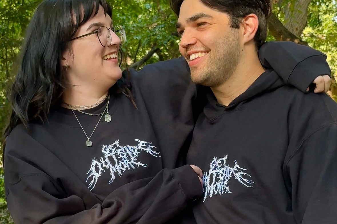 Two people wearing black hoodies with white text, standing close together outdoors.