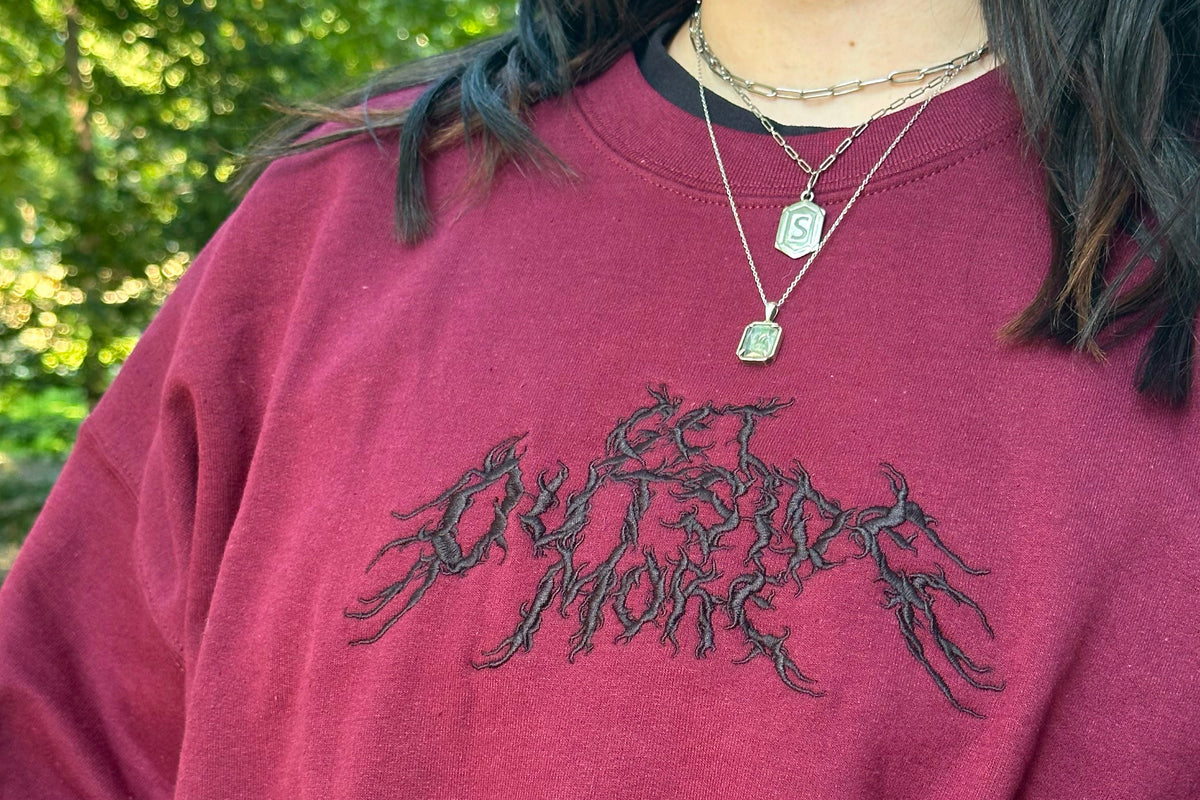 Person wearing a maroon sweatshirt with a black design outdoors