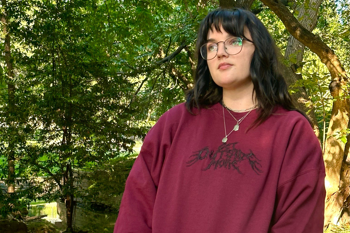 Person wearing a maroon sweatshirt with text in a forest setting