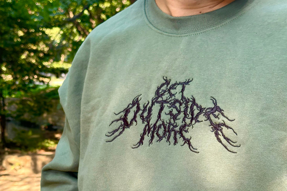 Person wearing a green sweatshirt with a black embroidered design outdoors.