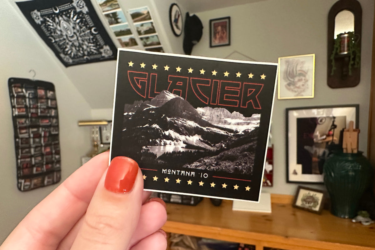 Hand holding a sticker with 'Glacier' design against a wall with posters and photos.