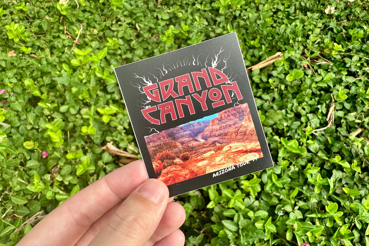 Hand holding a sticker with 'Grand Canyon' design against a green grass background