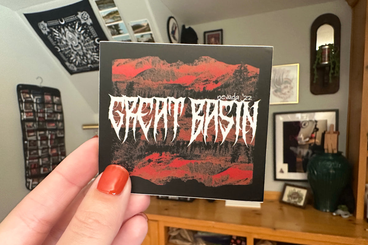 Hand holding a 'Great Basin' sticker in a room.