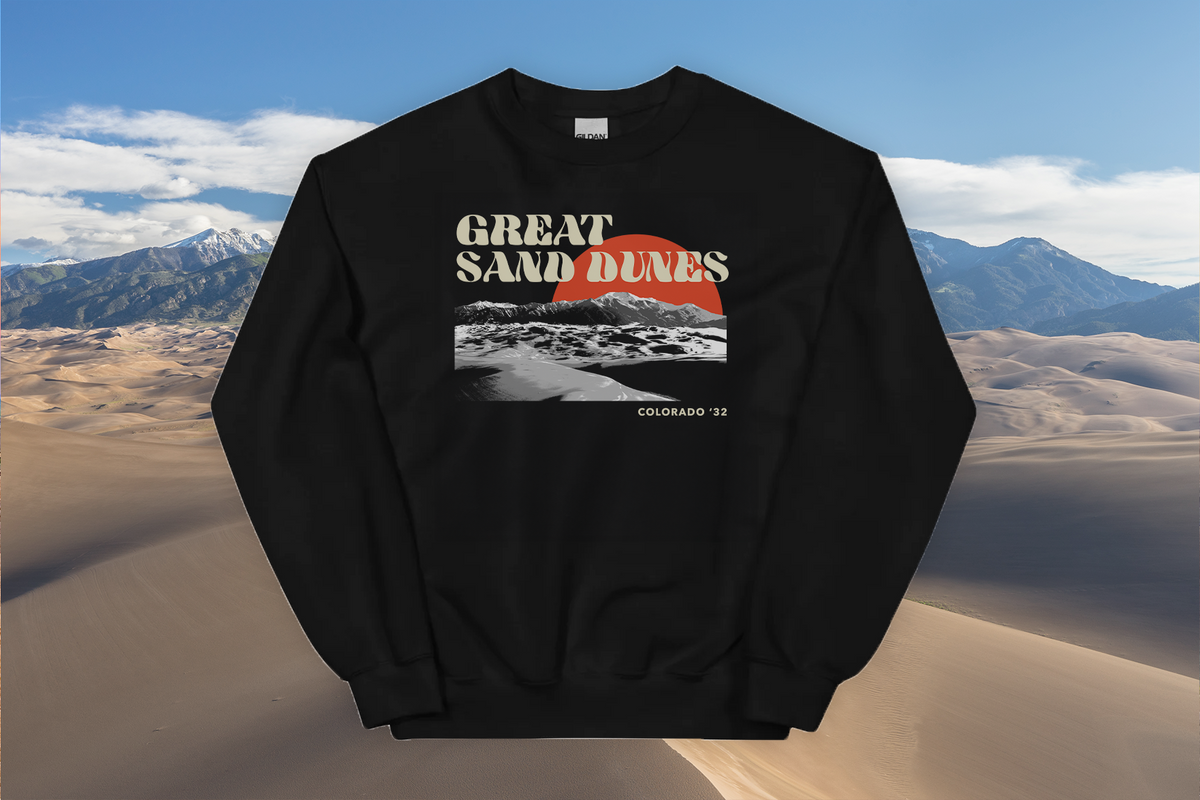 Black sweatshirt with 'Great Sand Dunes' design in front of sand dunes and mountains
