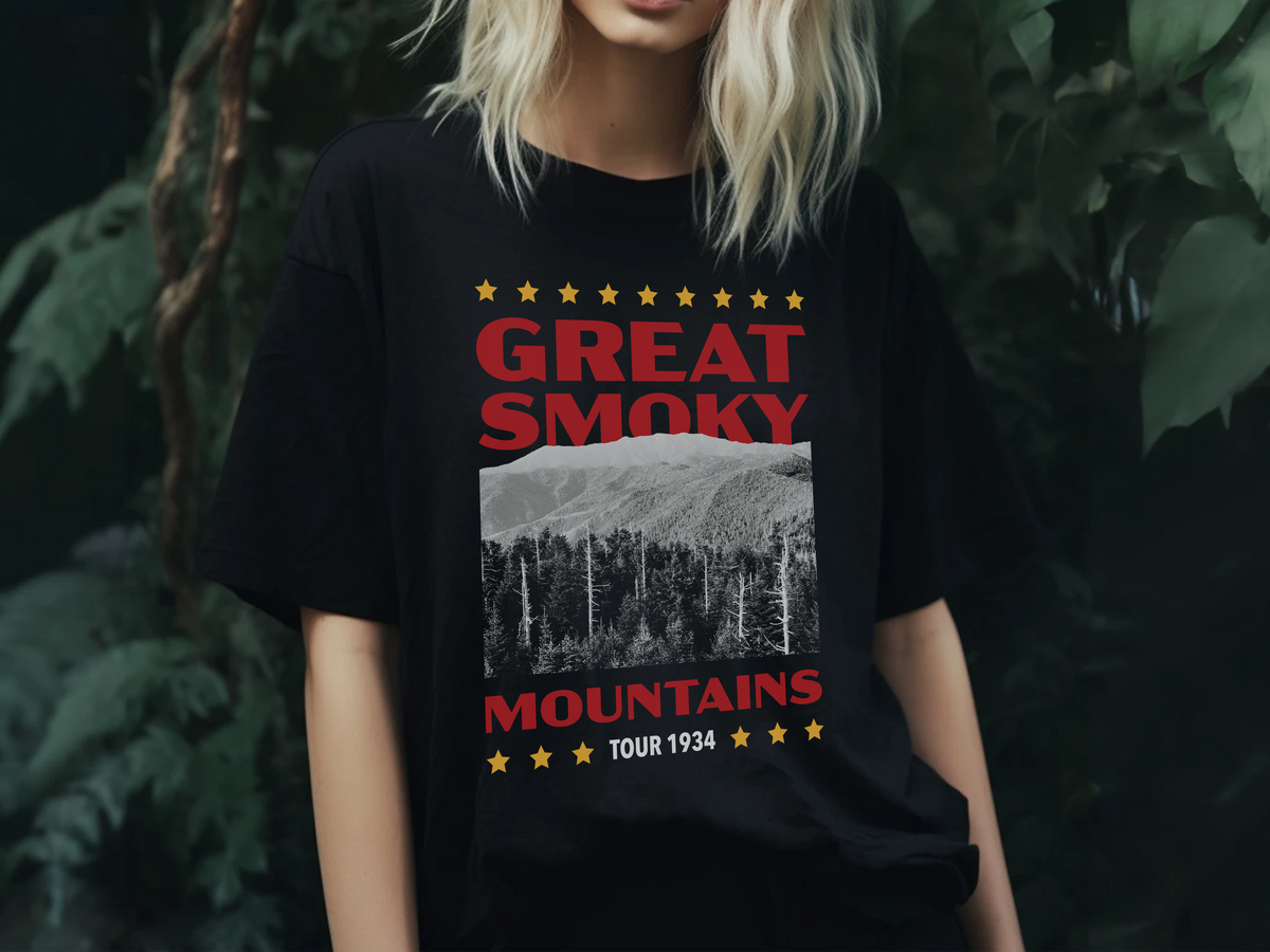 A person wearing a black t-shirt with a 'Great Smoky Mountains' design, in front of plants