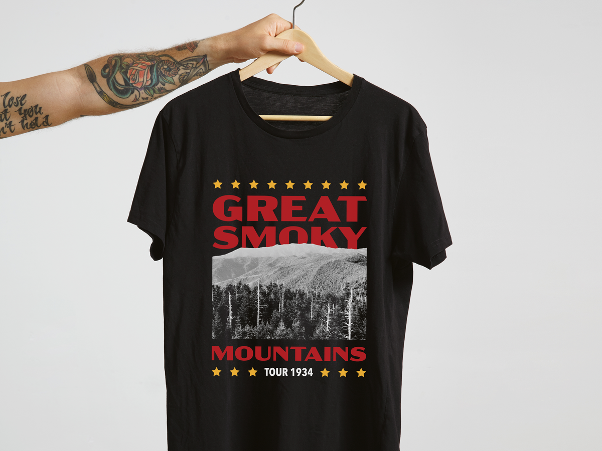 A black t-shirt with a 'Great Smoky Mountains' design, on a hanger in front of a white background