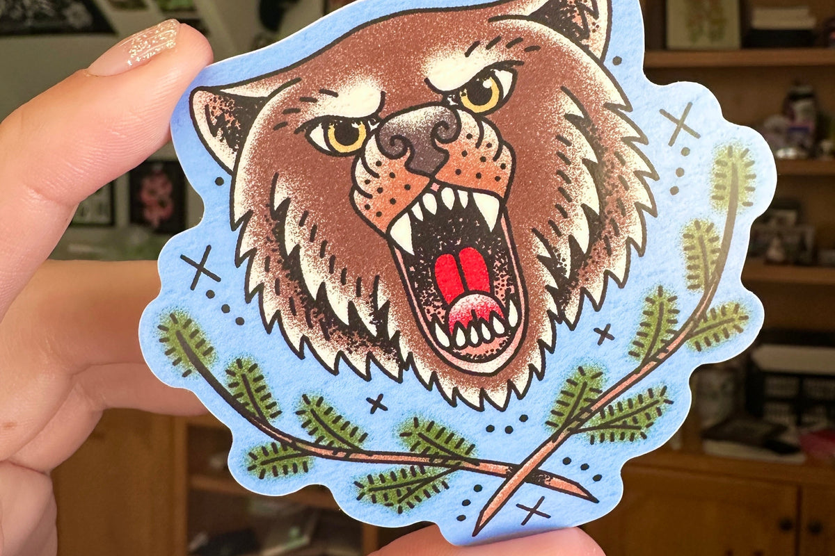 Sticker of a bear held by a hand with a blurred indoor background