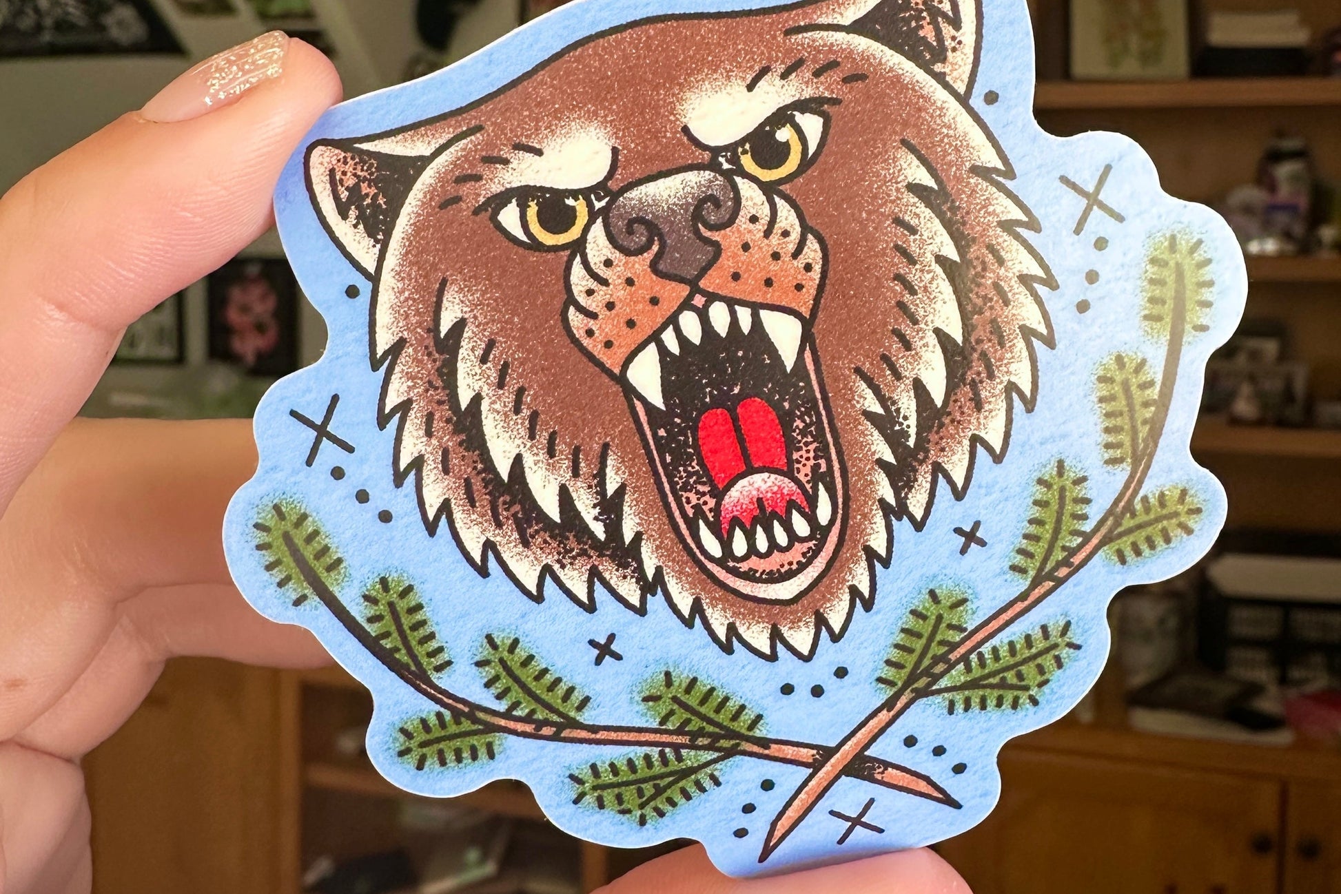 Sticker of a bear held by a hand with a blurred indoor background