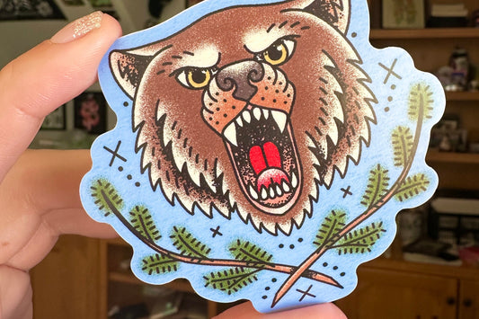 Sticker of a bear held by a hand with a blurred indoor background