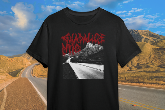 Black t-shirt with red 'Guadalupe Mountains' text and graphic, set against a scenic backdrop of a road and mountains.