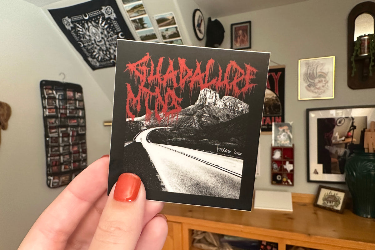 Person holding a 'Guadalupe Mountains' sticker in a room with various items on the wall.