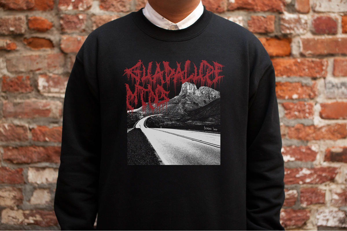 Person wearing a black sweatshirt with a 'Guadalupe Mountains' graphic design in front of a brick wall