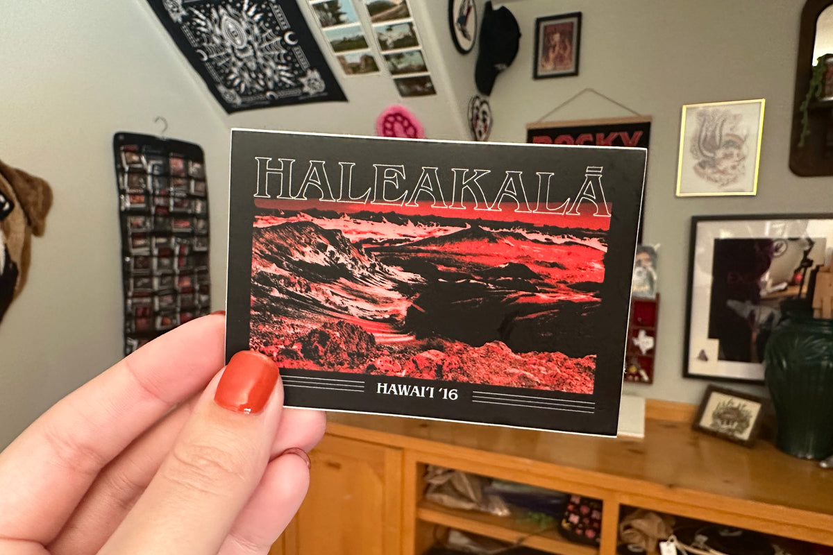 Person holding a Haleakala Hawaii sticker  in a room with various decorations.
