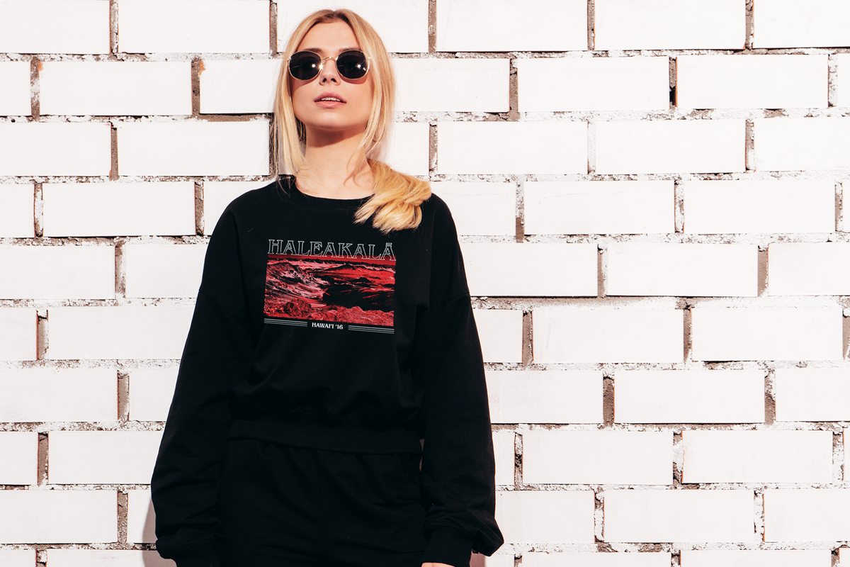 Person wearing a black sweatshirt with a 'Haleakala' graphic design against a white brick wall