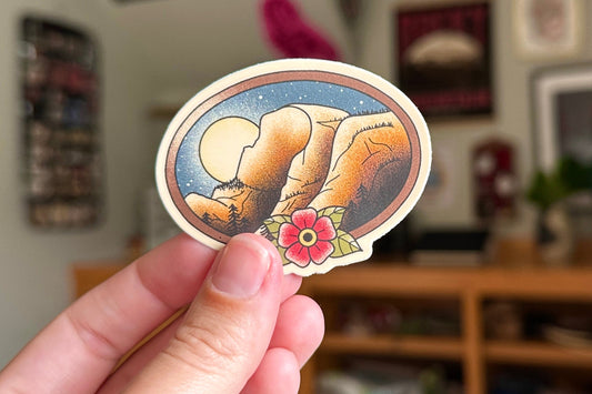 Hand holding a sticker with a design of a mountain and flower in a living room setting