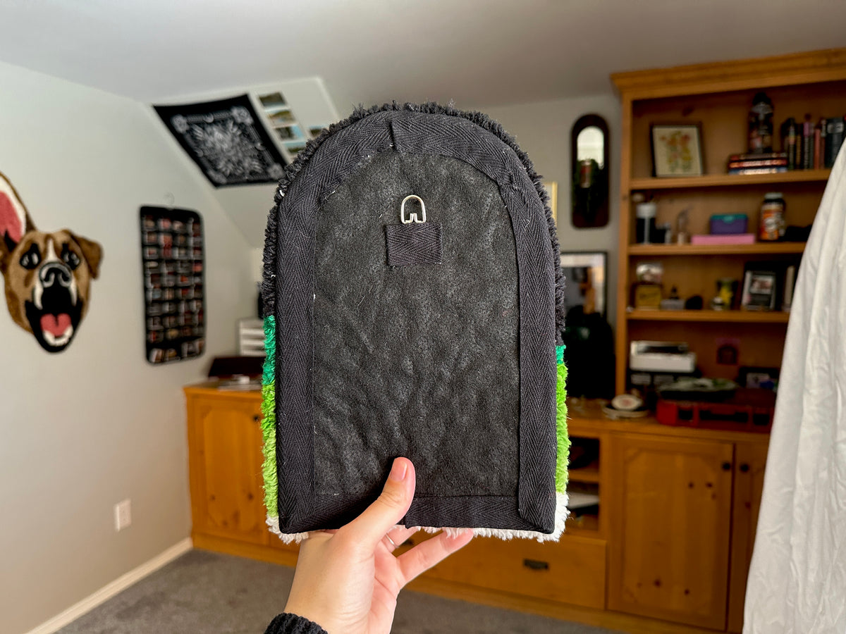 A person holding up the back of a tufted wall hanging in a room.