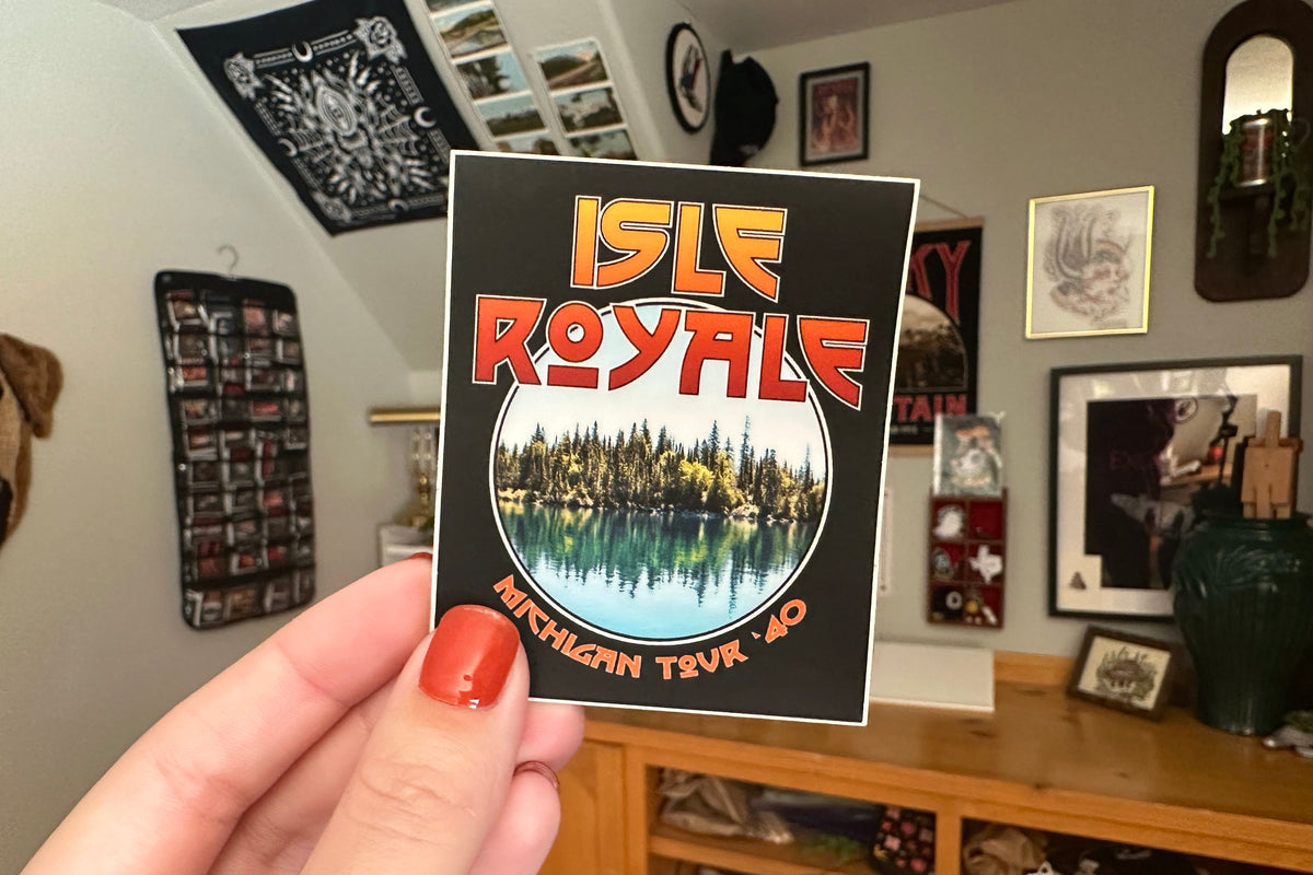 Hand holding a 'Isle Royale' sticker in a room with decor.