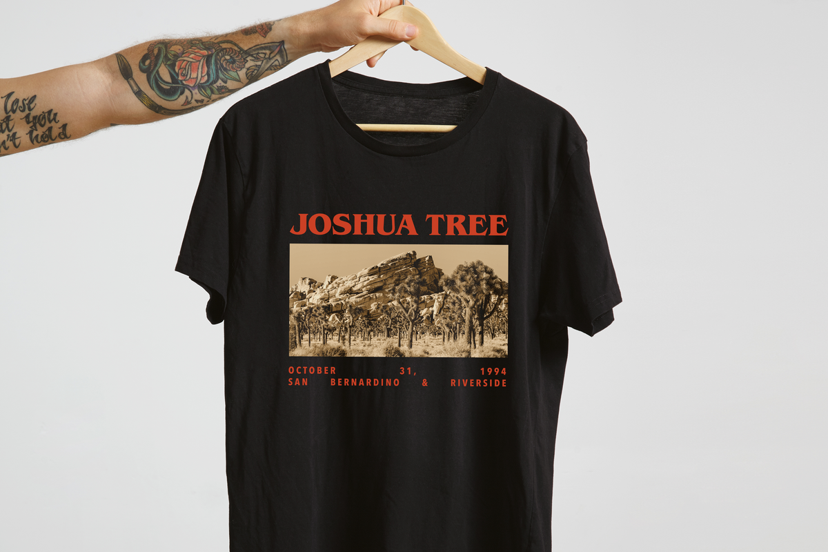 Black t-shirt with 'Joshua Tree' graphic design on a hanger against a light gray background