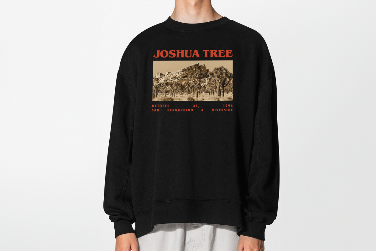 A person wearing a black sweatshirt with 'Joshua Tree' graphic design, in front of a white background