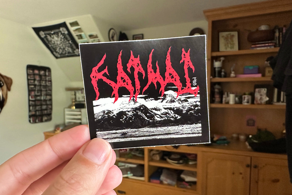 Person holding a sticker with red and black 'Katmai' design in a room with wooden furniture and decor.