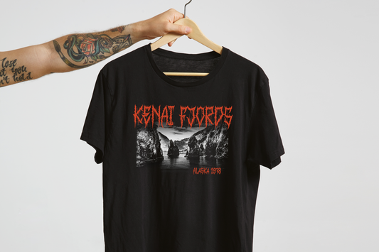 Black t-shirt with red and white 'Kenai Fjords' graphic design on a hanger against a light gray background
