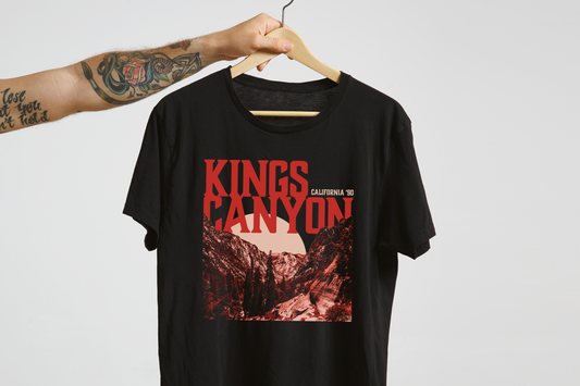 Black t-shirt with red 'Kings Canyon' text and graphic on a hanger against a light gray background